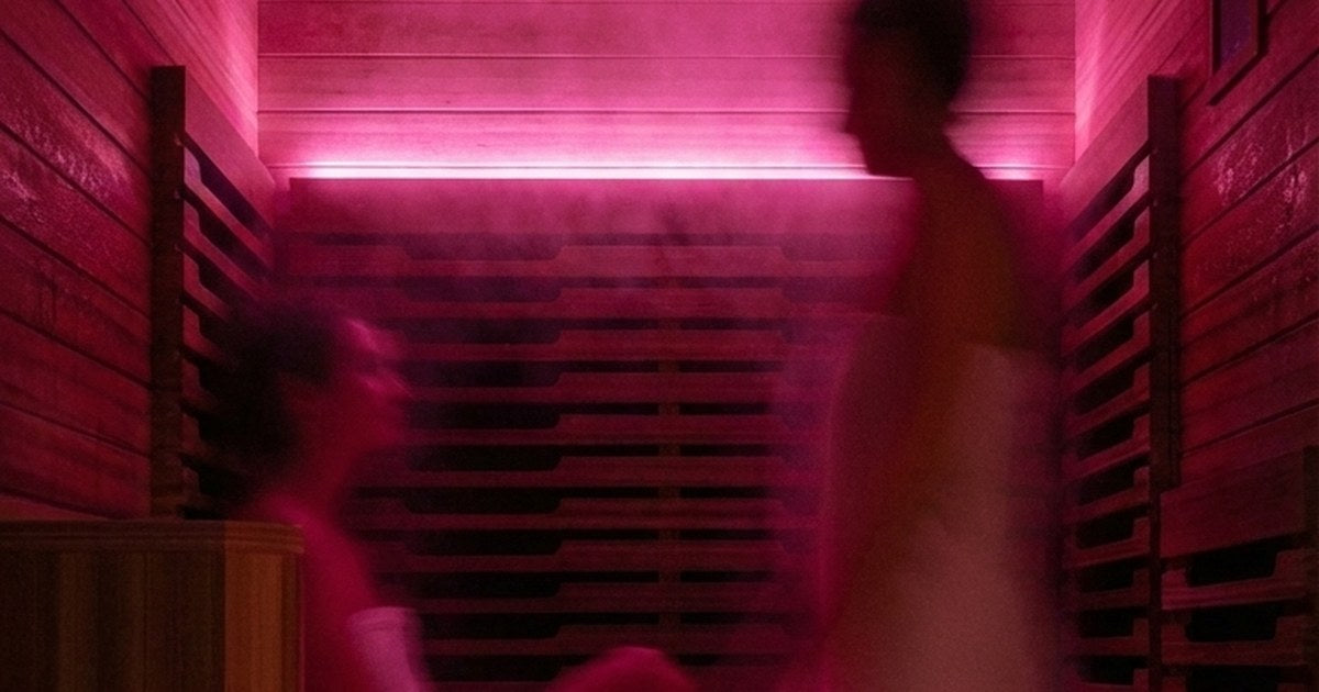 Person seated inside a sauna lit with deep pink chromotherapy light