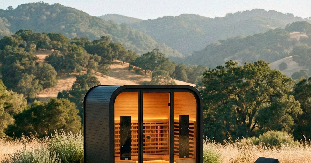 Rounded outdoor sauna pod lit in tall grass with rolling hills behind